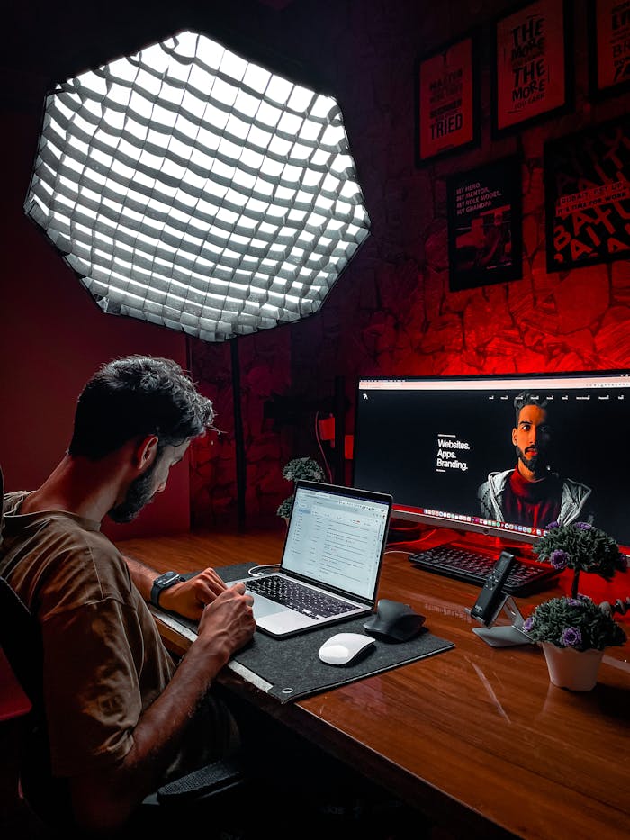 Mastering the First Impression: Your intriguing post title goes here Asian man working at a laptop in a stylish red-lit room with modern equipment and lighting.